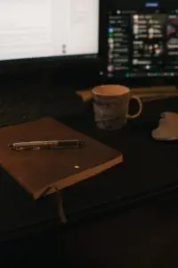 A leather notebook, a pen, and a coffee cup on computer desk